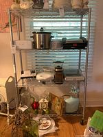 Full view of metal shelving unit showing four wire shelves and caster wheels, with various household items on shelves (not included)