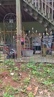 Wide shot showing several pieces of metal garden decor including the black Sheppard hooks and rusted metal trellis with leaf finials.