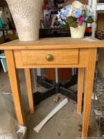 Front view of the wood side table showing the single drawer with decorative brass-colored round knob and four straight legs.