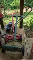 Earthwise tiller cultivator alongside two metal push mowers on a porch with garden backdrop.