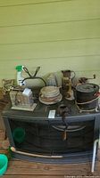 Wide view of vintage and antique kitchen tools including toaster, food mill, coffee grinder, kettle, and other metal kitchen items on a black stove base.