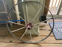 Full view of the antique metal wagon wheel showing the circular rim, spokes, and central hub on a wooden floor.