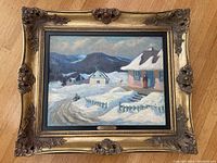 Frontal view of framed painting depicting a snow-covered rural landscape with mountains, ornate gold-tone frame
