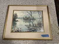 Full view of framed print featuring river scene with birch trees, held by a beige mat and gold frame.