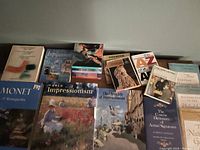 Box of art books arranged on a surface showing multiple titles related to impressionism, artist signatures, and world art masters