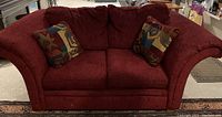 Front view of red loveseat with two multicolor geometric patterned throw cushions on a patterned rug.