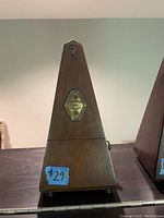Front view of wooden pyramid metronome with metal badge and blue price sticker $29.