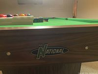 Close-up photo showing the 'National' brand logo on the side of the pool table with green felt surface and wood finish.