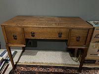 Front view of the solid oak desk showing the rectangular top, three drawers with metal drop pull handles, and tapered legs.