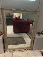 Front view of large vintage mirror with carved ornate cream frame showing interior reflection and tiled floor
