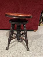 Front view of the vintage mahogany piano stool showing three turned legs with claw feet and round wooden seat.