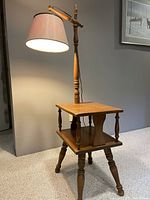 Photo of side table showing lamp lit with shade extended horizontally, turned wooden legs and top shelf with minor scratches.