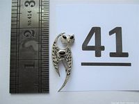 Top-down view showing the cat-shaped brooch next to a ruler indicating length of about 1.75 inches.