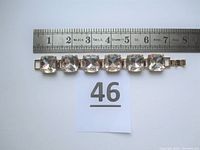 Gold tone bracelet with seven square clear crystals placed in individual settings, measured against a ruler showing length of approximately 7 inches, front view.