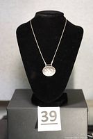 Photo showing sterling silver oval pendant hanging on a necklace bust display, to highlight shape and style.