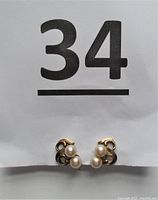 Front view of both screw back earrings showing two pearls on each gold mount beneath a lot number card
