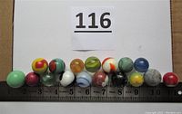 Seventeen shooter marbles laid out on ruler showing size from 0.9 to 1.05 inch