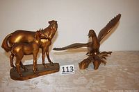 Photo of both gold leaf terra cotta sculptures: mare and colt horse pair on left and duck with wings spread on right on fabric surface with lot number card.