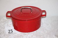 Red enameled Martha Stewart Dutch oven with handles and lid, on white patterned fabric background.