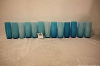 Front view of 13 blue opalescent glasses arranged in a line showing color variations and size.
