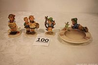 Photo showing all four Hummel figurines arranged side by side on table, capturing size and scale