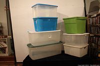 Seven plastic storage bins stacked showing various colors and sizes.