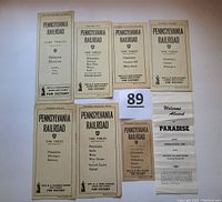 Seven Pennsylvania Railroad time tables and a brochure photographed on a white surface, showing covers and text details for each item.