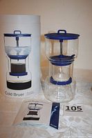 Photo showing the cold brew coffee maker assembled next to its original packaging and instruction manual.
