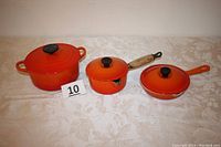 Overview of orange enamel three-piece cookware set: Dutch oven, saucepan and fry pan with lids