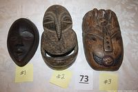 Three hand-carved wooden faces including two African masks and one painted Indonesian mask on white background