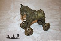 Front and side view of the vintage brass horse toy on wheels, showing detailed texture and rolling wheels.