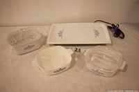 All four Pyrex Cornflower pieces are shown including rectangular covered dish, two casseroles, and warming tray on cloth surface.