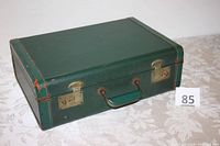 Exterior view of the closed green vintage suitcase with brass latches and handle, showing light wear and some rust on hardware.