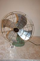 Front view of vintage Eskimo fan showing turquoise base, silver blades, and protective metal cage with Eskimo badge in center.