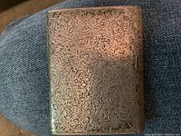 Engraved rectangular silver-hued metal case with scrolling floral pattern