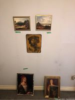 Full view of nine framed art pieces arranged on wall and floor showing varied subject matter and frame styles with wear and some damage