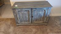Front and sides view of a gray weathered wood cabinet with two paneled doors and a metal latch lock.