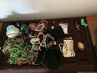 Photo showing a tray with various pieces of costume jewellery including bead necklaces in green and brown, faux pearl bracelets, and a cluster of assorted costume items.