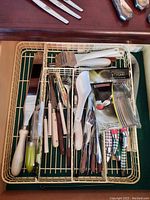 Photo of cutlery drawer showing knives, forks, graters, plastic handles, and a packet of plastic forks