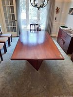 Overall view of rectangular wood dining table from one end, showing tabletop and one plinth base.