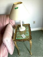 Full view of side table and lamp positioned next to a pink upholstered couch on a green carpeted floor.