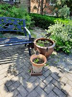 Photo showing large brown pot and smaller pots with decorative chair in background.