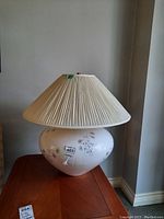 Full view of a table lamp showing the ceramic base with floral design and pleated fabric shade on a wooden surface.