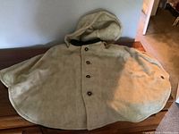 Full view of the beige Loden wool cape with hood laid flat showing its size and shape.