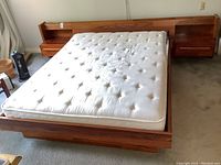 Front view of bed frame with tufted mattress installed, showing wood base and floating headboard with nightstands attached