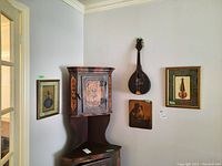 Wide view showing two framed musical art prints and the stringed musical instrument on the wall above a corner cabinet.