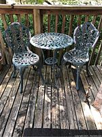 Full view of the outdoor patio set showing the table and two chairs with worn green paint and detailed lattice design.
