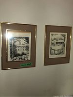 Two black-and-white prints framed with beige mats and gold-tone frames hung on a white wall