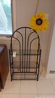 Black metal rack with arched top and several shelves, positioned against a wall.