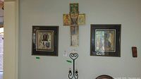 Photo showing the entire arrangement: two framed religious icons, a cross-shaped religious wall art with a rosary, and a black metal candle sconce mounted below.